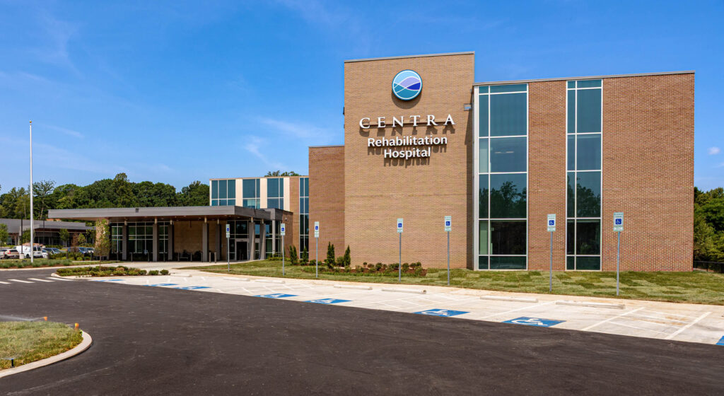Exterior view of Centra Rehabilitation Hospital building with brick facade and large glass windows under a clear blue sky.